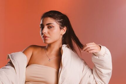 Stylish woman poses in a beige down jacket against a warm-toned background.