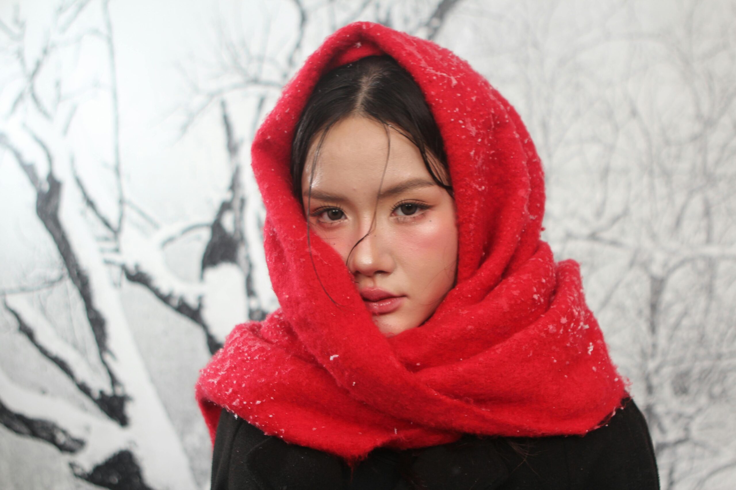 Close-up portrait of a woman in a red scarf against a snowy backdrop.